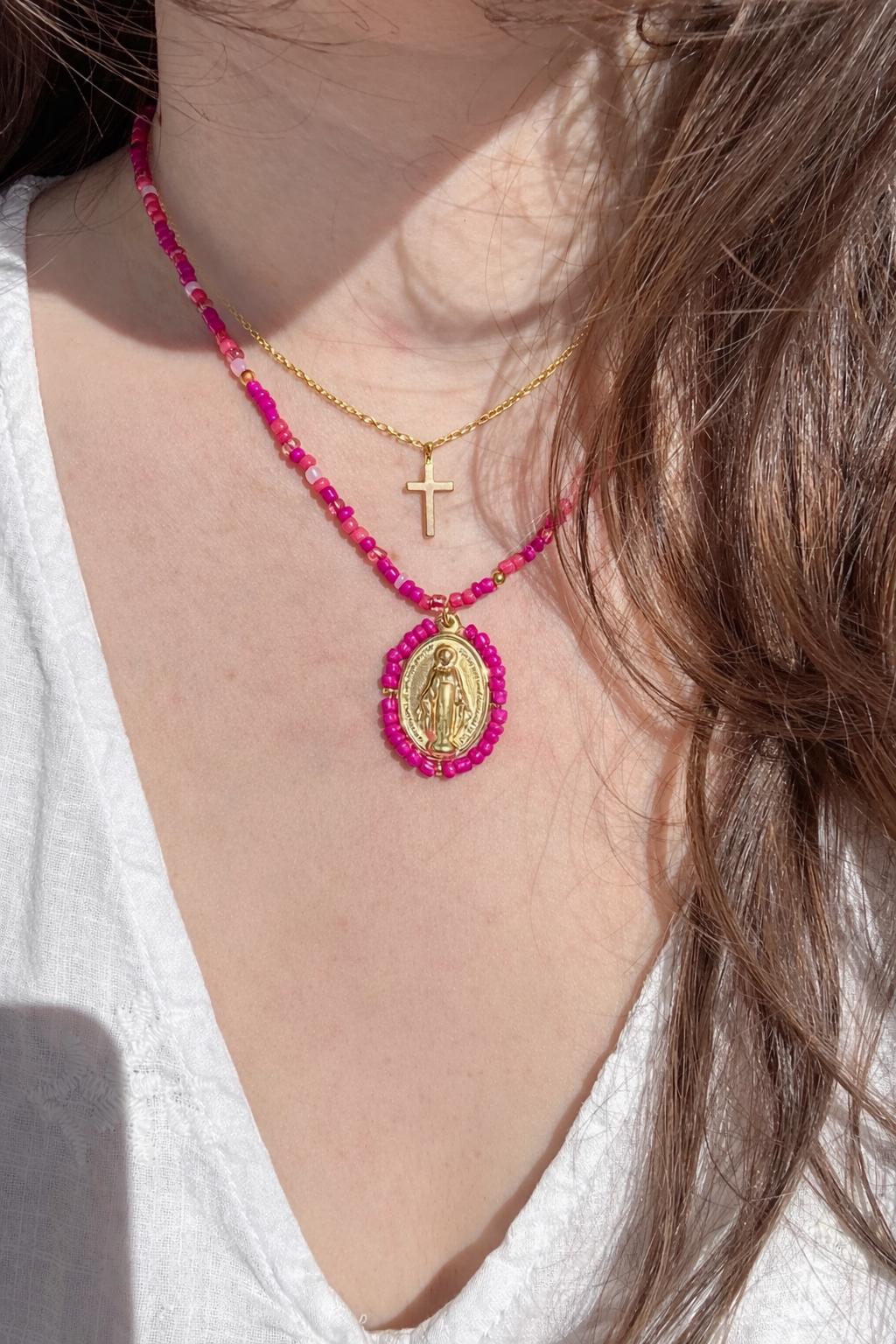 Femme portant un collier Médaille Miraculeuse perlée rose fuchsia et une croix dorée