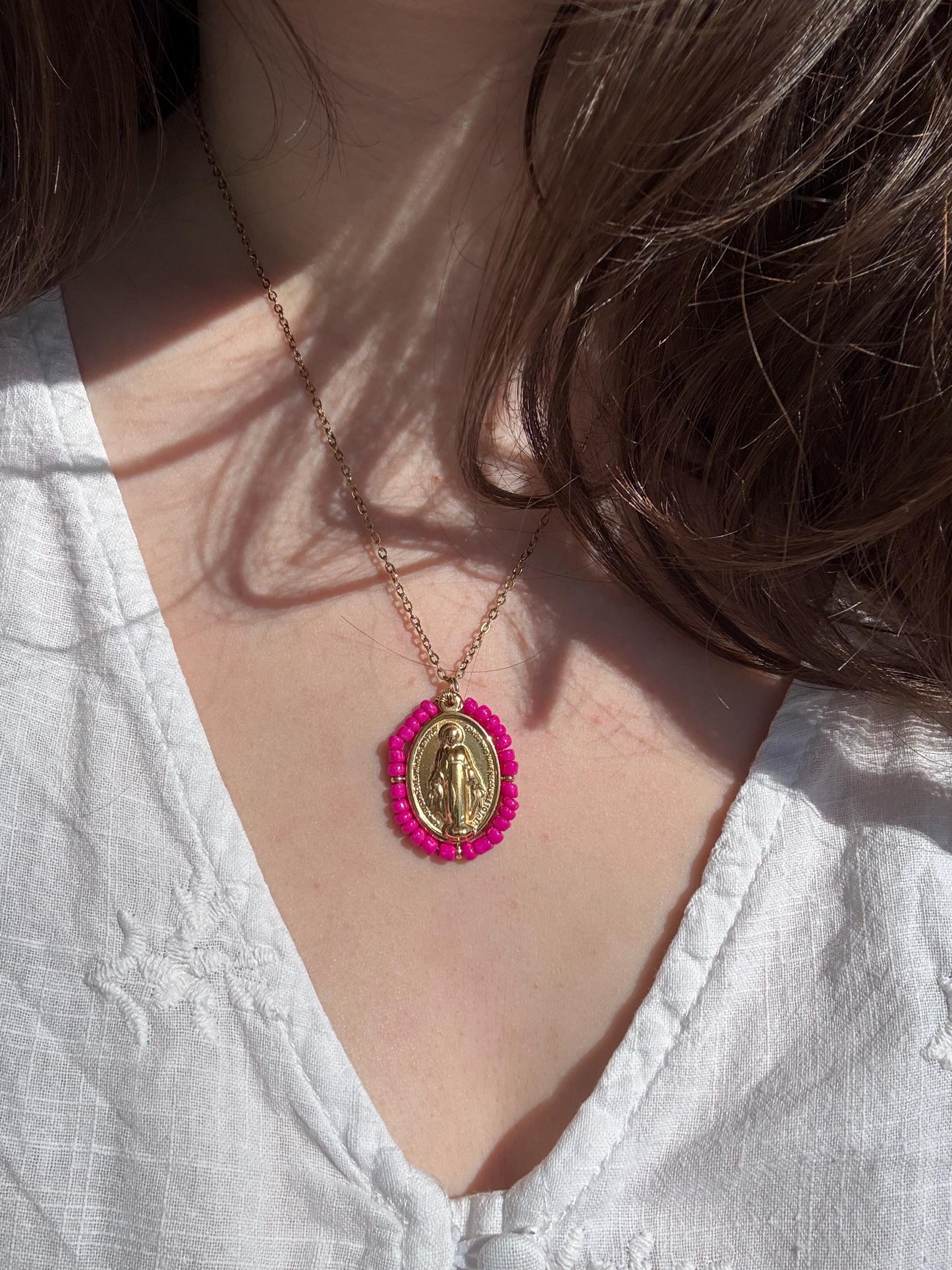 Femme portant un pendentif Médaille Miraculeuse perlée rose sur chaîne dorée